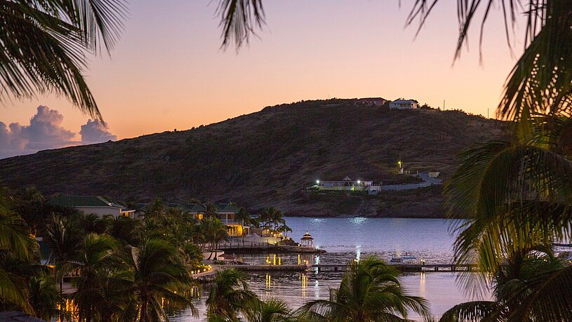 Bucht vor Antigua im Sonnenuntergang mit Blick auf romantisch beleuchtete Hafenstädte, Palmen und das Meer Bucht vor Antigua im Sonnenuntergang mit Blick auf romantisch beleuchtete Hafenstädte, Palmen und das Meer