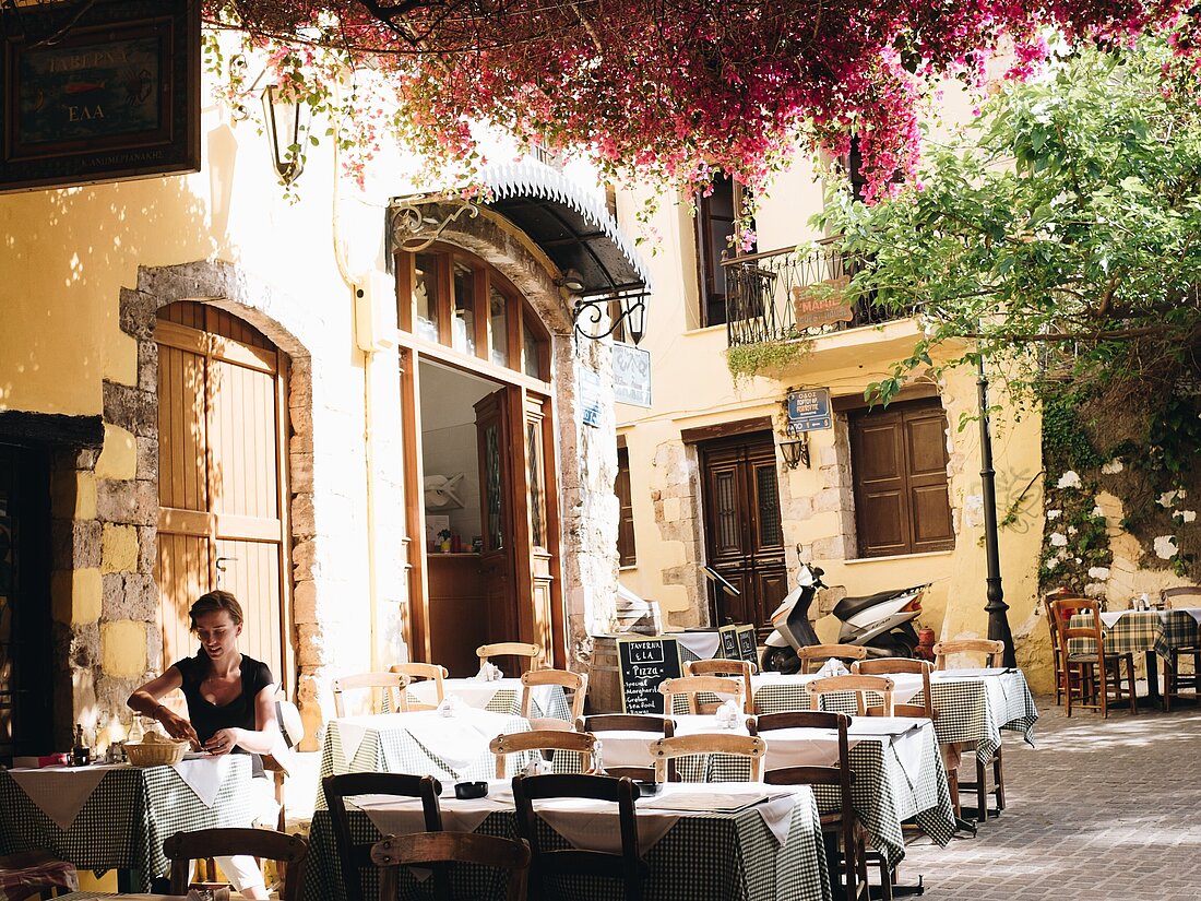 Eine Frau sitzt in einer Taverna in einer Gasse in einer Griechischen Stadt