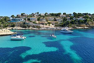Boote ankern in einer Bucht über türkisblauem Wasser vor einer grünen Insel.