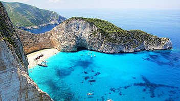 Bucht mit weißem Sandstrand und Schiffswrack umrandet von hohen Klippen mit türkisblauem Wasser davor