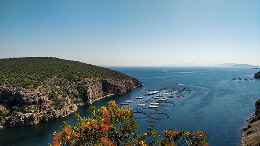 Blick von einer Anhöhe auf Steinbucht bei Epivadros, umgeben von blauem Meer und Segelyachten