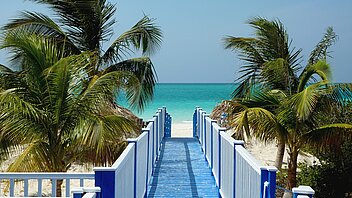 Strand in Kuba Weißer Sadnstrand zwischen Palmen und Meer mit blauem Steg