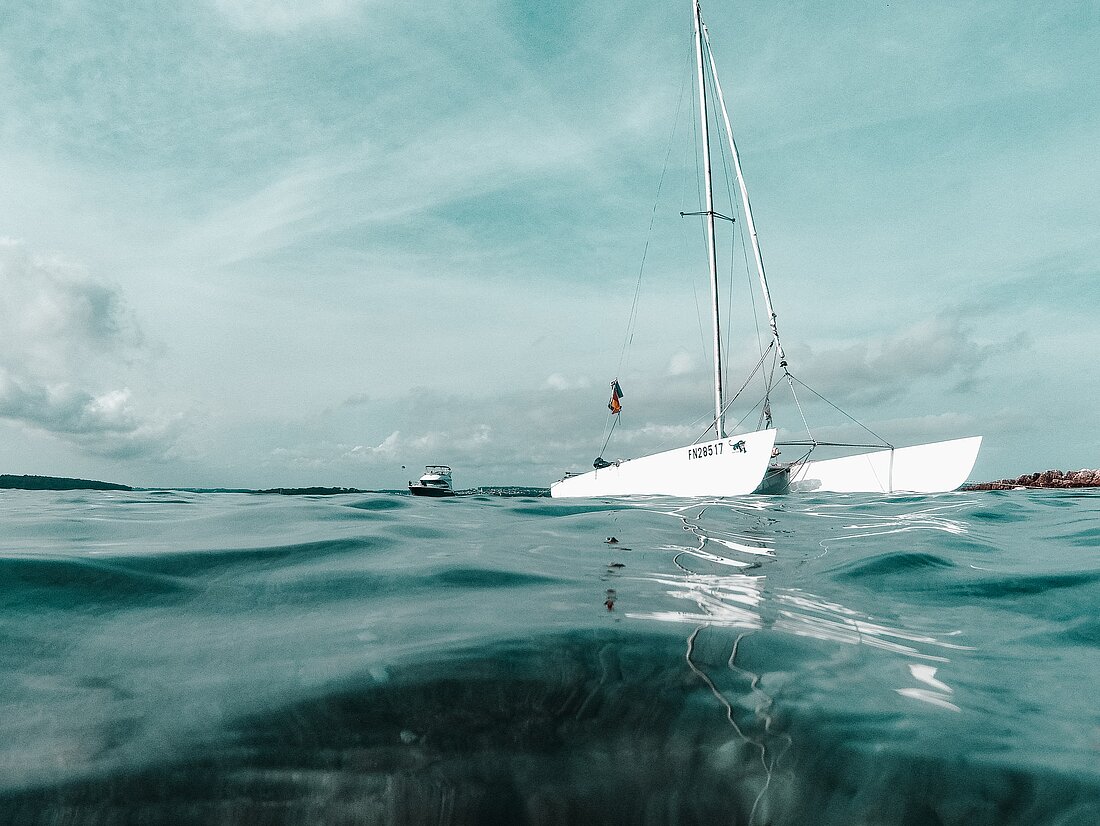 Blick vom Wasser auf Katamaran und Segelyacht vor Istrien bei bewölktem Himmel