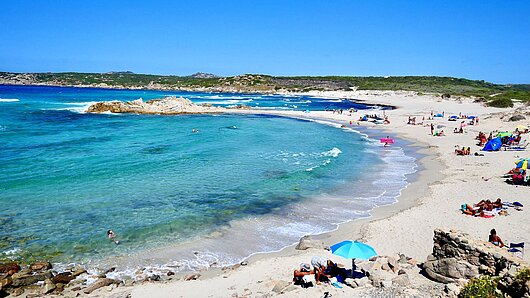 touristischer Sandstrand Nordsardiniens mit türkisem Wasser, bei sonnigem Wetter