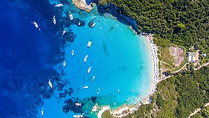 Blick von oben auf Paxos, umgeben von grüner Landschaft und türkisem Meer mit einigen Yachten und Booten