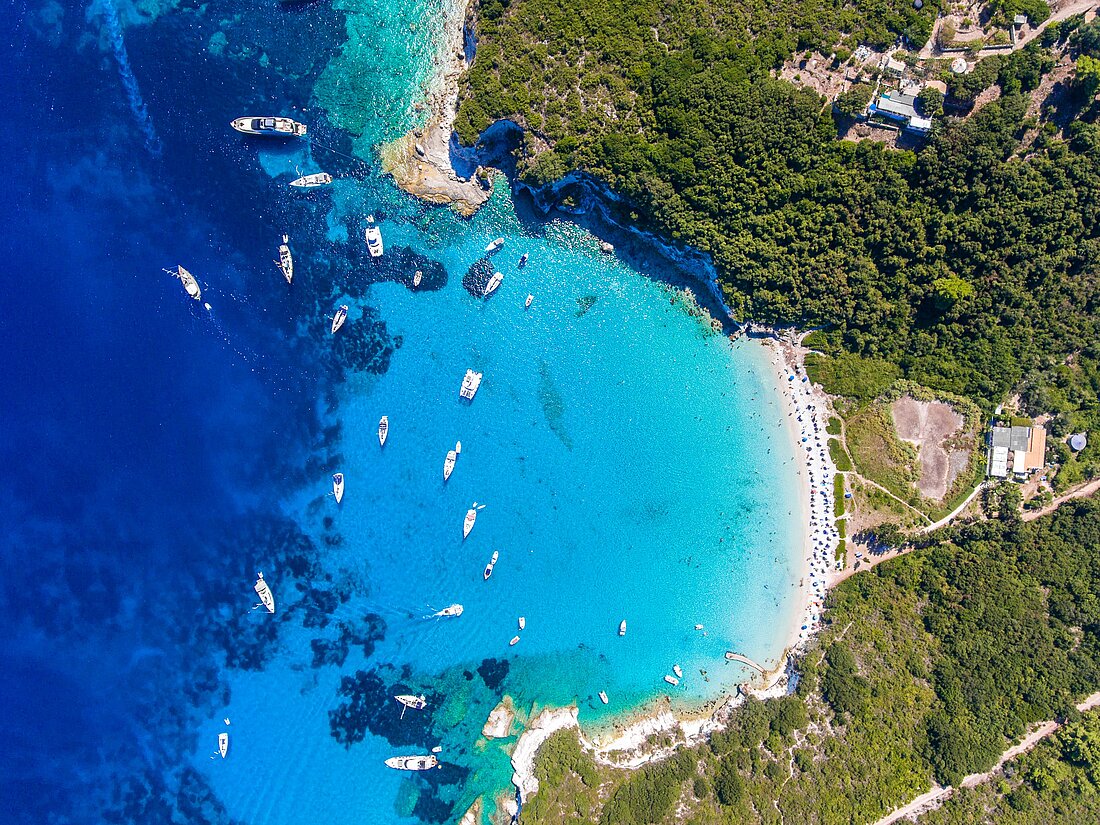 Blick von oben auf Paxos, umgeben von grüner Landschaft und türkisem Meer mit einigen Yachten und Booten