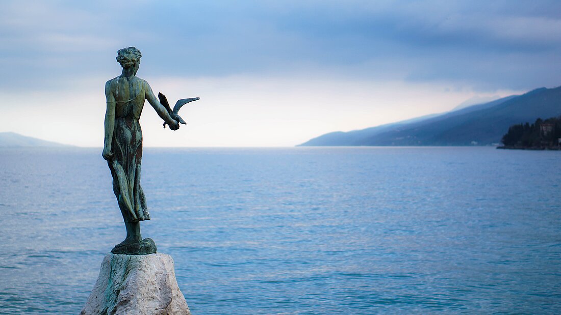 Statue auf einem Stein an der Küste Kroatiens und Blick auf das Meer und den Horizont Statue auf einem Stein an der Küste Kroatiens und Blick auf das Meer und den Horizont