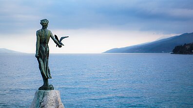 Statue auf einem Stein an der Küste Kroatiens und Blick auf das Meer und den Horizont