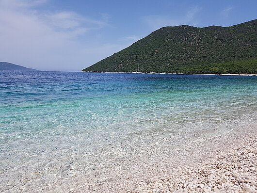 Blick vom Kieselstrand auf türkises Wasser vor Kefalonia