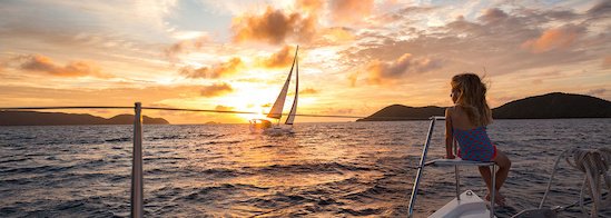 Blick aus einer Segelyacht auf ein kleines Mädchen am Bug, eine Segelyacht und den Sonnenuntergang, sowie das Meer Blick aus einer Segelyacht auf ein kleines Mädchen am Bug, eine Segelyacht und den Sonnenuntergang, sowie das Meer